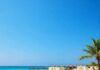 Dreamy Beach Resorts You Can’t Miss This Summer Wide-angle beach with resort cabanas and azure water.